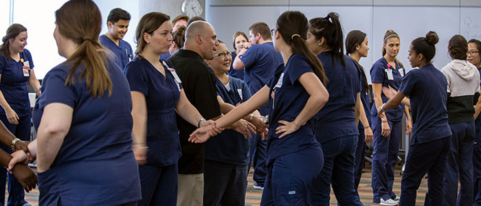 Candid image of a group of class attendees standing together, some attendees grabbing others by the wrist, while practicing an exercise