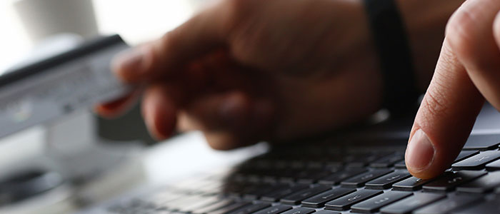 Close-up image of keyboard and hands, with left hand entering information and right hand holding a credit card