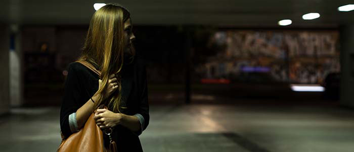 Frightened solitary woman clutching purse in a dimly lit parking garage