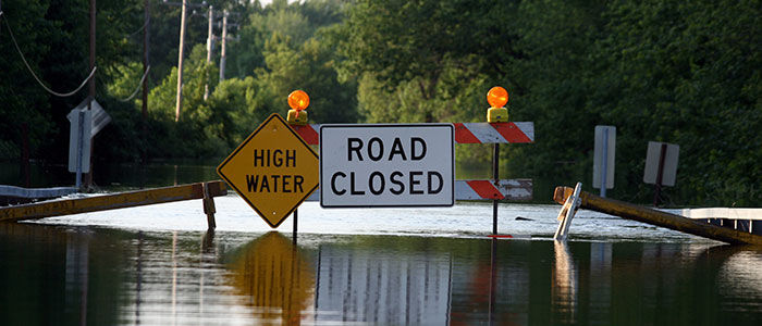 Flooded road with High Water and Road Closed signs on a barrier across it