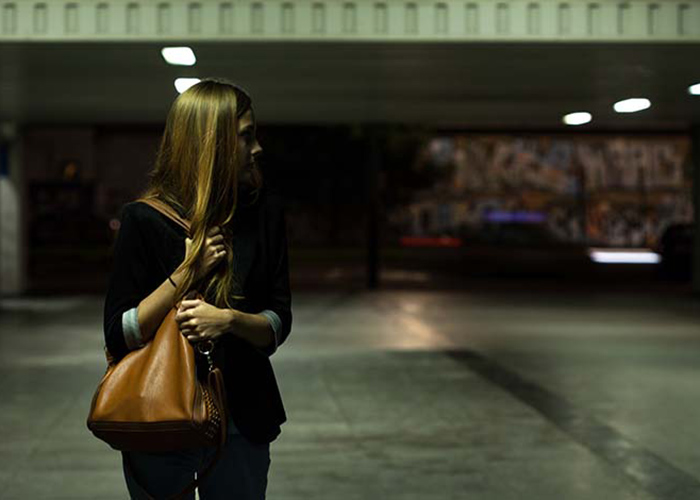 Frightened solitary woman clutching purse in a dimly lit parking garage